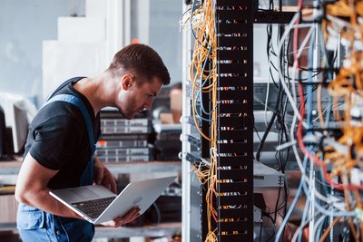 Service Management Mann mit Laptop vor Schaltschrank