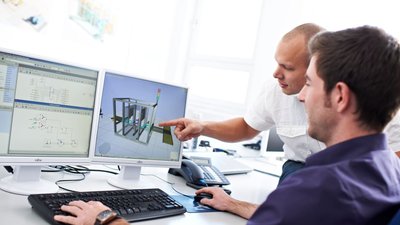Gemeinsames Problemverständnis trotz Komplexität Zwei Mitarbeiter vor Monitoren mit komplexen Programmierungen