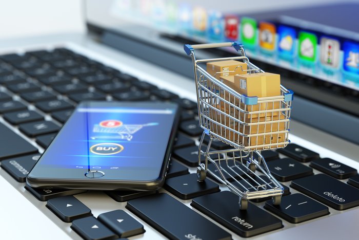 Headerbild: Smartphone mit Shopping-App auf Tastatur liegend, Einkaufswagen mit Paketen
