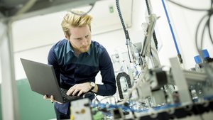 Qualitätsmanagement in der Produktion mit mobilen Anwendungen Mann mit Laptop führt Inspektion an Maschine durch