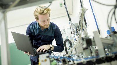 Qualitätsmanagement in der Produktion mit mobilen Anwendungen Mann mit Laptop führt Inspektion an Maschine durch