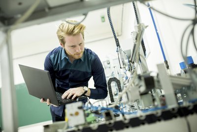 Mann in der Produktion mit Laptop und mobilen Anwendungen Mann mit Laptop vor Maschinenkulisse